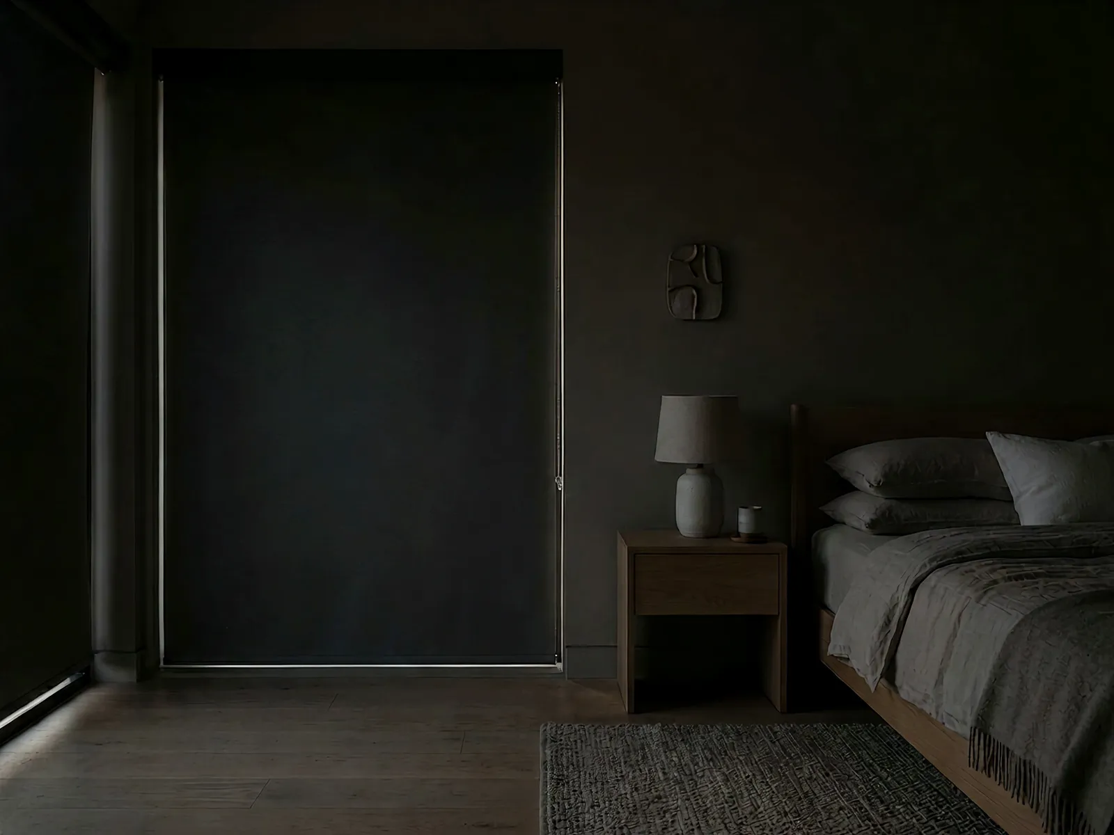 Bedroom at night with a blackout shade fully lowered, only a soft glow from the side window