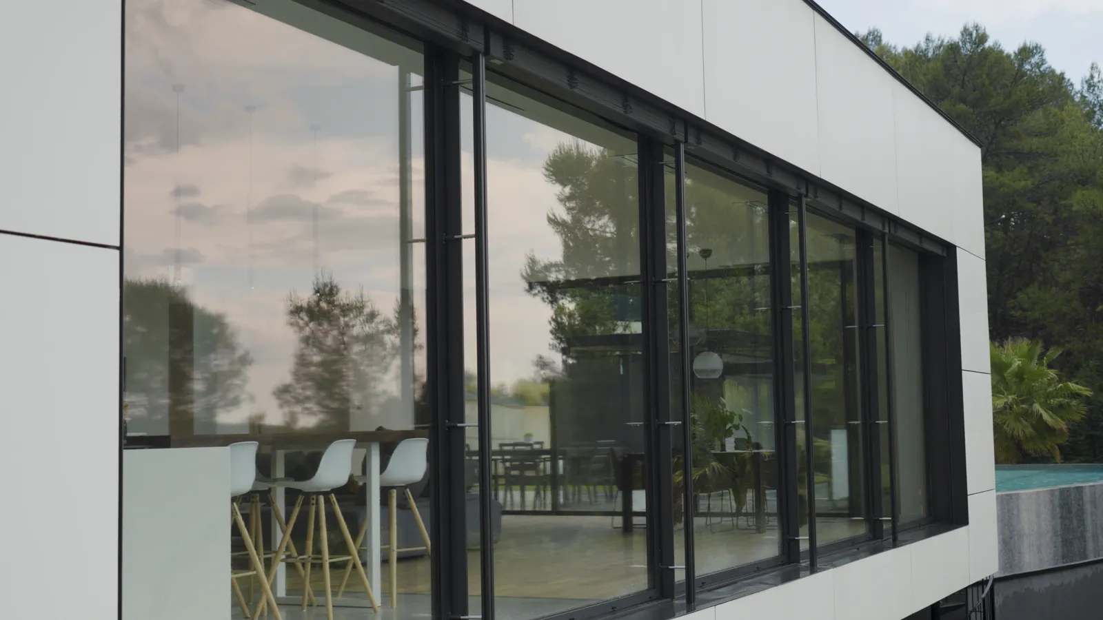 Exterior of a modern home with motorized slat blinds fully raised over floor-to-ceiling glass